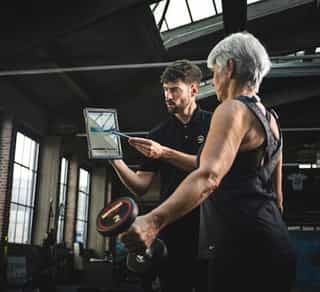 Trainer von Physiosport mit Tablet eläutert einer Frau das Training.