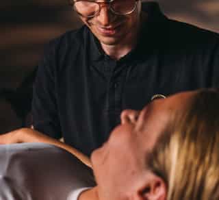 Physiotherapeut von Physiosport Köln mit Frau im Gespräch. Die Frau liegt auf einer Behandlungsliege.er Nackenmuskulatur.