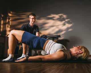 Mitarbeiter von PhysioSport unterstützt Patientin beim Training der Rumpfmuskulatur.