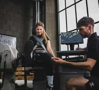 Trainer von Physiosport Köln erläutert Sportlerin Kraftübungen für die Beinmuskulatur an einem Trainingsgerät.