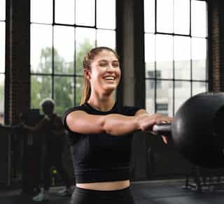 Zu sehen ist eine Sportlerin bei PhysioSport, die Kraftübungen mit Kugelhantel für die Verbesserung der Rumpfmuskulatur macht und dabei lächelt.