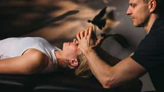 Trainer mobilisiert Kopfmuskulatur einer Patientin.