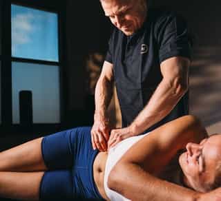 Osteopathie: Therapeut von PhysioSport behandelt die Hüfte einer Patientin, die entspannt seitlich auf einer Liege liegt..