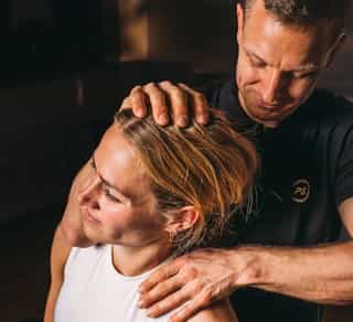 Patientin sitzt entspannt bei PhysioSport auf einer Liege, Physiotherapeut führt osteopathische Nackenbehandlung durch.