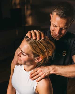 Trainer mobilisiert Nackenmuskulatur einer Patientin.