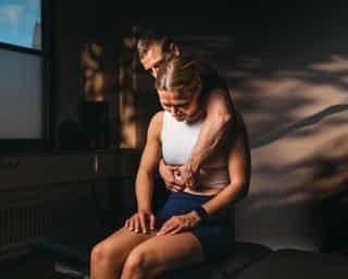 Trainer mobilisiert Wirbelsäule einer Patientin.