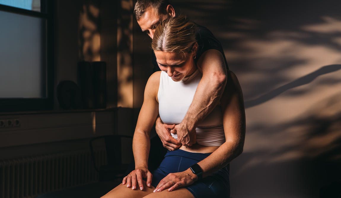 Trainer von PhysioSport Köln mobilisiert die Wirbelsäule einer Patientin.