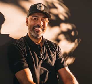 Das Bild zeigt einen Mitarbeiter von Physiosport Kölan, der lächelnd auf einem Fahrrad sitzt.