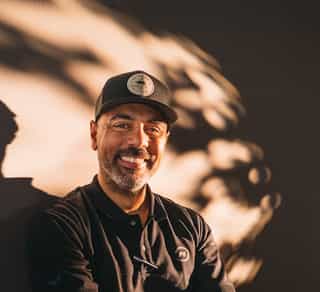 Das Bild zeigt einen Mitarbeiter von Physiosport Kölan, der lächelnd auf einem Fahrrad sitzt.