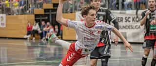 Das Bild zeigt eine Szene aus einem Handballspiel der Herrenmannschaft vom Longericher SC Köln, den Partnern von Physiosport. Zu sehen sind Spieler auf dem Spielfeld und Zuschauer im Hintergrund.