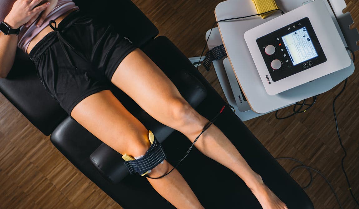 Patientin liegt auf Liege bei PhysioSport, Elektroden am Knie für Elektrotherapie in der Physikalischen Therapie, Gerät daneben.