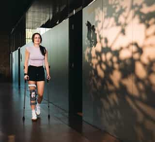 Junge Sportlerin mit Krücken und Kneebrace auf dem Weg zur Behandlung bei PhysioSport Köln.