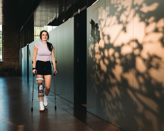 Junge Sportlerin mit Krücken und Kneebrace auf dem Weg zur Behandlung bei PhysioSport Köln.