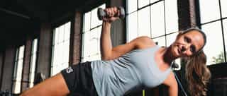 Zu sehen ist eine Sportlerin bei therapeutischen Übungen gegen Schulterluxation. Seitstütz mit abgewinkeltem Arm und kleiner Kurzhantel, auf der Tainingsanlage von Physiosport Köln.