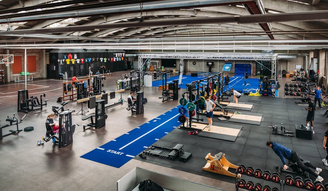 Zu sehen ist die große Trainingsanlage von PhysioSport Köln mit Matten, Geräten und Menschen, die daran trainieren.