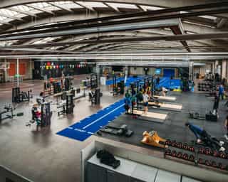 Zu sehen ist die große Trainingsanlage von PhysioSport Köln mit Matten, Geräten und Menschen, die daran trainieren.