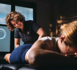 Das Bild zeigt eine Physiotherapeutin, die eine Patientin behandelt. Die Patientin liegt auf einer Behandlungsliege.