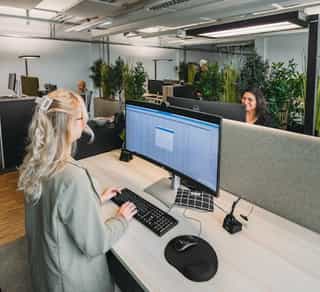 Zu sehen ist der Einblick in einen offenen Arbeitsplatz bei Physiosport Köln. Dort sitzt eine Mitarbeiterin am Computer und im Hintergrund andere Arbeitsplätze.