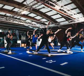 Zu sehen ist ein Gruppe von Patienten bei Physiosport Köln, die gerade Gruppentraining in einer Trainingshalle mit blauem Boden durchführen.