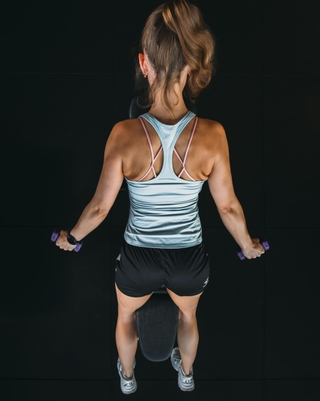 Zu sehen ist eine Sportlerin von hinten, insbesondere der Rücken, bei einem speziellen Rückentraining bei PhysioSport Köln.