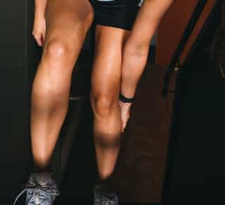 Sportlerin fasst sich vor Schmerzen an ihre Wade und Achillessehne.