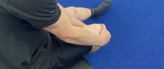 Man sieht einen Sportler bei PhysioSport Köln, schräg von hinten und oben gesehen, der sich vor Schmerzen an sein Knie fasst.