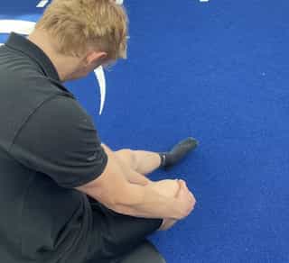 Man sieht einen Sportler bei PhysioSport Köln, schräg von hinten und oben gesehen, der sich vor Schmerzen an sein Knie fasst.