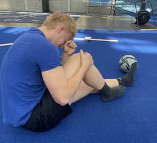 Zu sehen ist ein Sportler schräg von hinten gesehen bei PhysioSport Köln, der sich vor Schmerzen an sein Knie fasst.