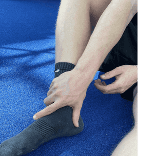 Sportler sitzt mit Schmerzen am Boden bei PhysioSport Köln und fasst sich an sein Sprunggelenk.