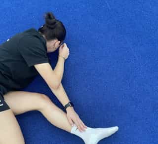 Sportlerin liegt mit Schmerzen am Boden bei PhysioSport Köln und fasst sich an ihr Sprunggelenk.