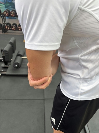 Man sieht einen Sportler mit Schmerzen am Ellenbogen, Tennisellenbogen Behandlung bei PhysioSport Köln.