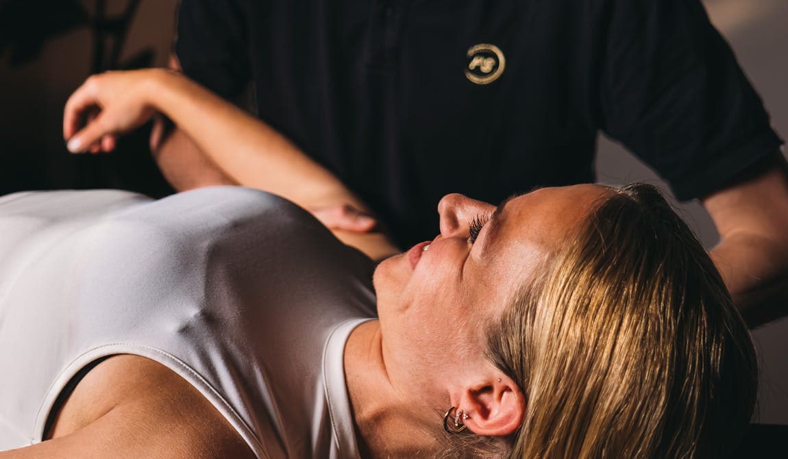 Physiotherapeut von PhysioSport Köln behandelt eine Sportlerin mit manueller Therapie lächelnd.
