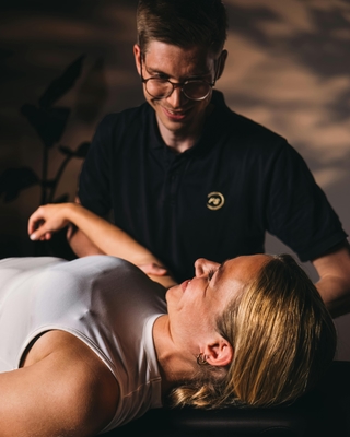 Physiotherapeut von PhysioSport Köln behandelt eine Sportlerin mit manueller Therapie lächelnd.