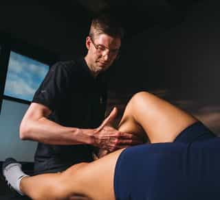 Physiotherapeut von PhysioSport Köln behandelt eine Sportlerin mit manueller Lymphdrainage an der rechten Wade.