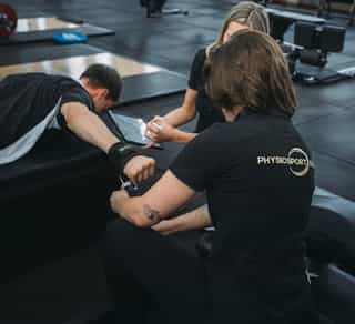 Zwei Physiotherapeuten von PhysioSport Köln mit Patient im Einzelgespräch und Behandlung bei Schulterbeschwerden.