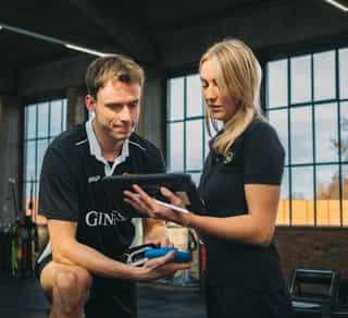 Zu sehen ist eine trainerin von PhysioSport Köln beim Beratungs- und Therapiegespräch mit einem Sportler.